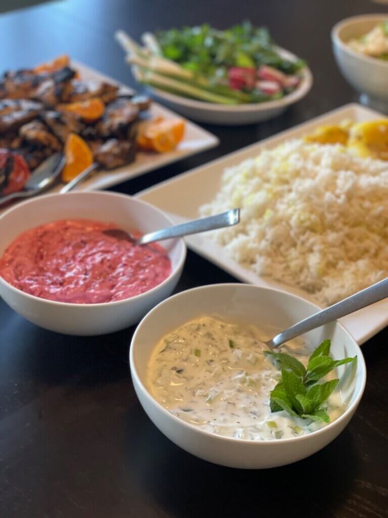 Side view of Persian yogurt and cucumber dip with rice, grilled chicken, and fresh herbs