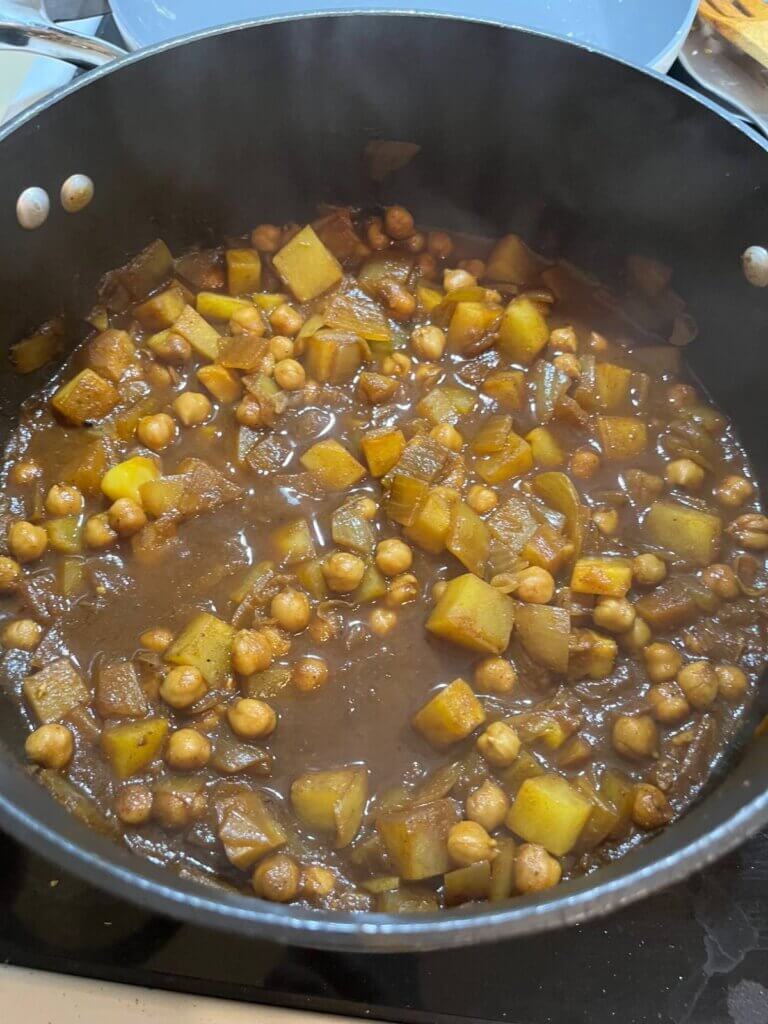 Vegan Gheymeh simmering in a pot with chickpeas, potatoes, and rich tomato sauce.
