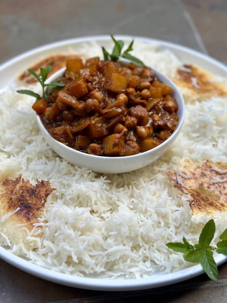 A bowl of vegan chickpea and potato Gheymeh served with Persian basmati rice and golden tahdig, garnished with fresh herbs.