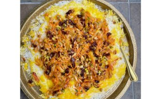 Close-up of Jeweled Persian Rice (Javaher Polo) topped with caramelized onions, shredded carrots, dried cherries, golden raisins, apricots, pistachios, and almonds on saffron rice