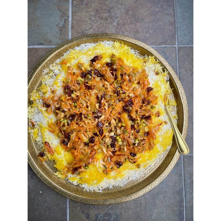 Close-up of Jeweled Persian Rice (Javaher Polo) topped with caramelized onions, shredded carrots, dried cherries, golden raisins, apricots, pistachios, and almonds on saffron rice
