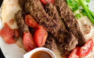 Persian pan kabab, or kabab tabei, served with flatbread, tomatoes, herbs and dipping sauce
