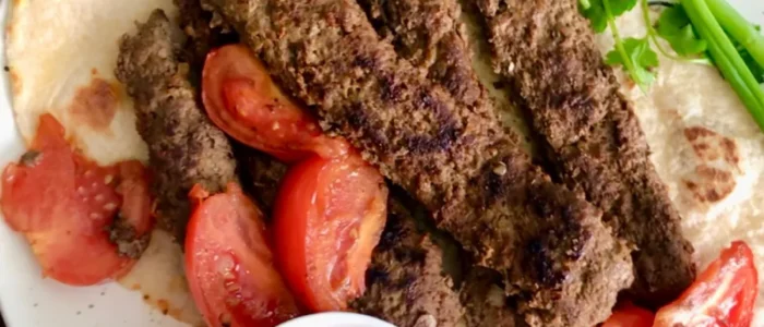 Persian pan kabab, or kabab tabei, served with flatbread, tomatoes, herbs and dipping sauce