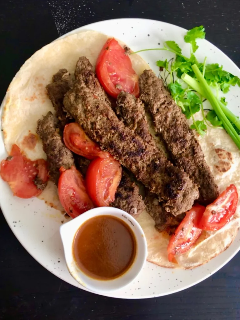 Persian pan kabab, or kabab tabei, served with flatbread, tomatoes, herbs and dipping sauce